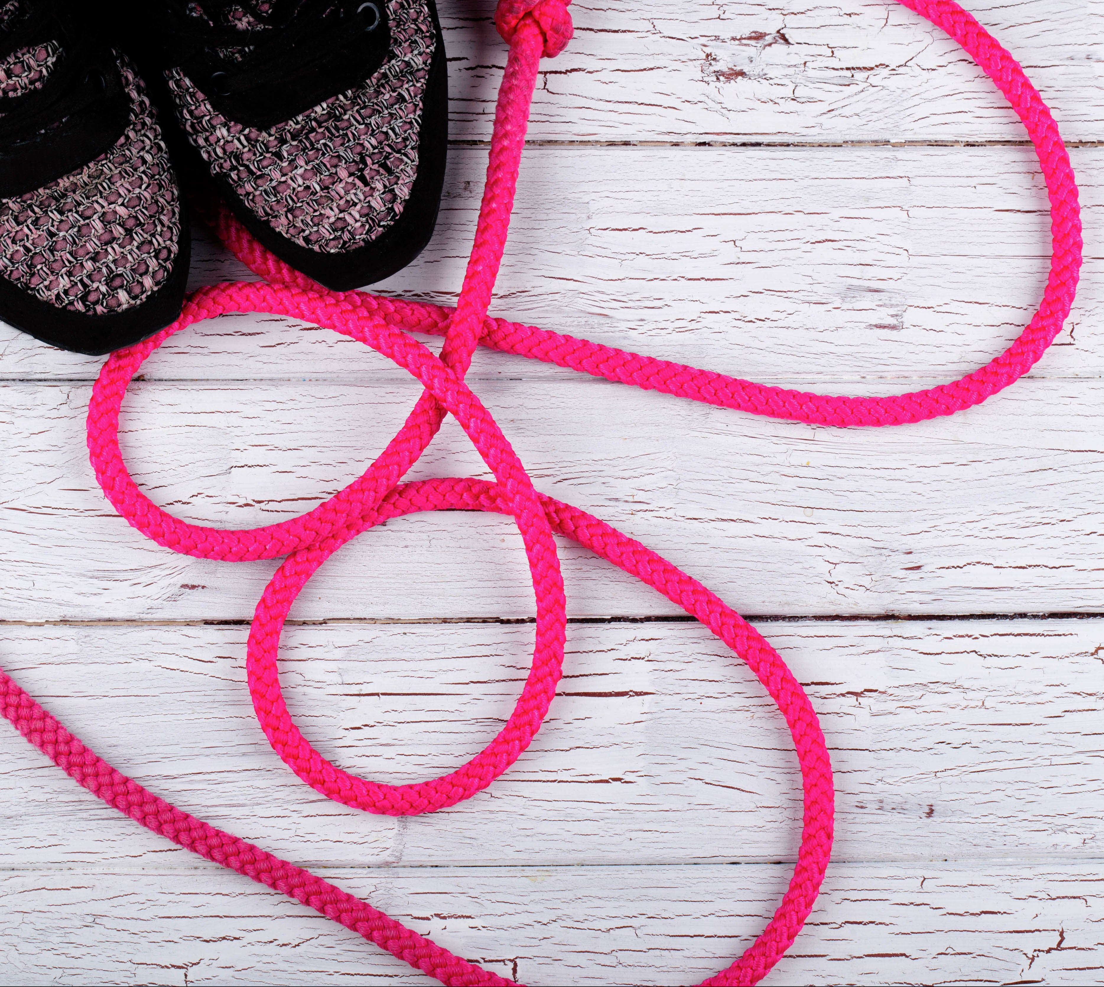 Pink jump rope lies by black snickers on white floor